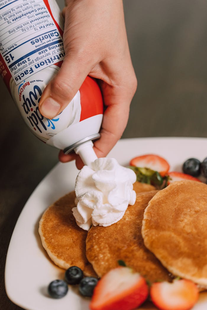 Close-up of pancakes topped with whipped cream and fresh berries on a plate. Perfect for breakfast.